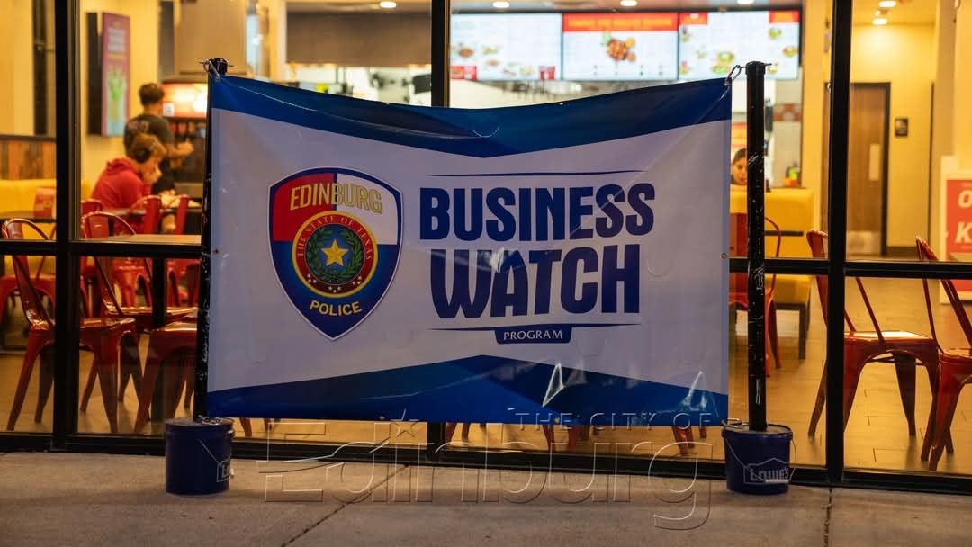 Large banner displayed indoors reading &ldquo;Business Watch Program&rdquo; with the Edinburg Police logo, set up in front of a restaurant seating area.
